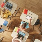 Kinder sitzen an ihrer Schulbank mit PCs und digitalen Tablets für Aufgaben; Gorodenkoff - adobe stock