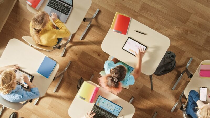 Kinder sitzen an ihrer Schulbank mit PCs und digitalen Tablets für Aufgaben; Gorodenkoff - adobe stock